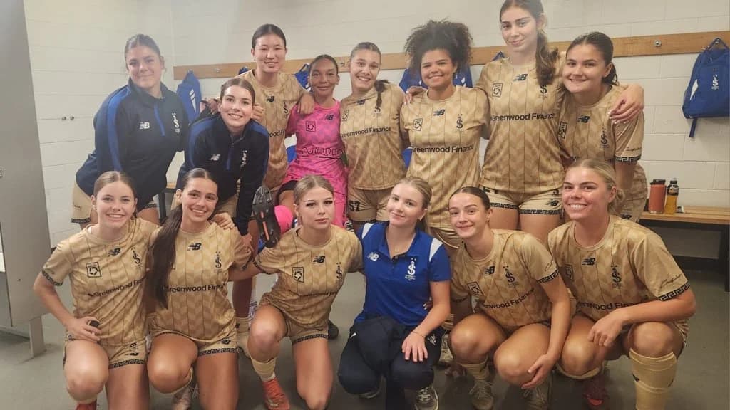 The Sydney Olympic FC U18 Girls squad together in the dressing room in their gold away kit, Greenwood Finance across the front of the jersey.